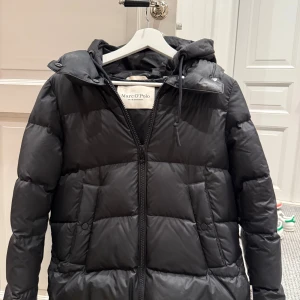 Svart dunjacka från Marc O'Polo - Snygg svart dunjacka från Marc O'Polo med huva och dragkedja framtill. Jackan är quiltad och har två fickor med knappstängning. Perfekt för kalla dagar och har en klassisk, stilren look som funkar till det mesta. Nypris 2200:-