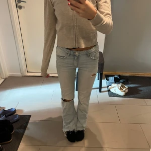 Lågmidjade jeans  - Säljer dessa ljusblåa lågmidjade bootcut jeans från ginatricot, med snygga hål/slitningar på benen. Köpta på 14+ avdelningen i storlek 152. Passar mig perfekt som vanligtvis har storlek 32, xs. Fina knappar på fickorna baktill.  Skick 10/10, sparsamt använda.  Köpte de för 399kr för ett par år sedan, tror inte de säljs längre. 