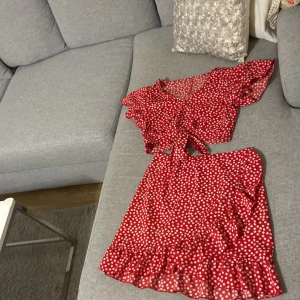 Röd blommig omlottkjol med volang - Säljer en röd kort omlottkjol med vita små blommor och volangkant. Kjolen har en feminin och flowy look, perfekt för dig som gillar färg och mönster. Materialet känns lätt och luftigt, och den knyts i sidan för en snygg passform.passar storlek 34-38. Använd 1 gång .tror märket är shin.materialet behöver inte strykas den faller fint mycket fint 