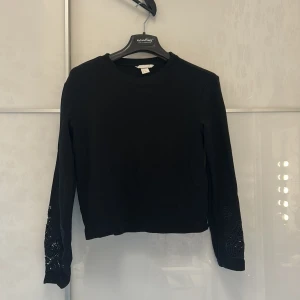 Svart långärmad tröja med broderi - Svart långärmad tröja från H&M med snygga broderade detaljer. Tröjan har en rund hals och är tillverkad i mjuk bomull, perfekt för dig som gillar stilrena plagg med en twist. Passar dig som vill ha något enkelt men ändå unikt.