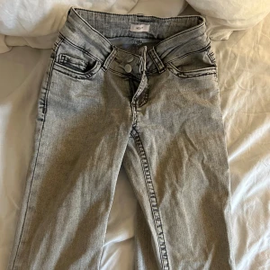 Grå jeans från Nelly - Snygga grå jeans från Nelly med svarta kontrastsömmar och broderade bakfickor. Jeansen har klassisk femficksdesign, dragkedja och knapp framtill. Materialet är denim och färgen är ljusgrå med tvättad look. Perfekta för en avslappnad streetstil. Defekter syns i bilderna