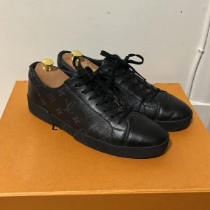 Svarta Louis Vuitton sneakers i skinn - Säljer dessa äkta svarta Louis Vuitton sneakers i skinn med klassiskt monogrammönster i mörkgrått. Använda ett fåtal gånger. Skorna har rund tå, platt sula och snörning. Lyxig och stilren design som passar perfekt till en exklusiv stil. Levereras med originalbox, dustbag och kvitto. Hör av dig vid funderingar, kan gå ner i pris!! Nypris 5000kr