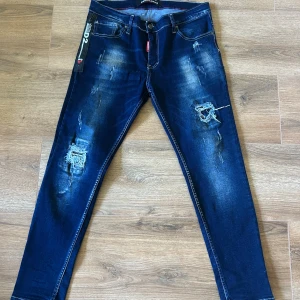 Mörkblå distressed jeans Dsquared2 - Snygga mörkblå jeans från Dsquared2 med slitna detaljer och trasiga partier på låren. Modellen har smal passform, klassisk femficksdesign och tydliga slitningar för en cool look. Perfekta för dig som gillar streetstyle och vill sticka ut.
