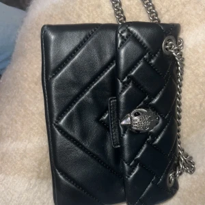  Kurt Geiger märkesväska - Snygg svart axelväska från Kurt Geiger med quiltad design och silverfärgad kedja. Väskan har ett unikt fågelhuvud som spänne och är tillverkad i skinn. Perfekt storlek för det viktigaste och ger en cool vibe till din outfit. Älskar denna väska men har påriktigt använt den 1-2 gånger då jag är en guld tjej🥰
