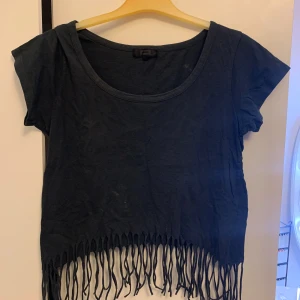 Svart fransad topp från Bik Bok - Svart croppad topp från Bik Bok med korta ärmar och rund hals. Nederkanten har långa fransar som ger en cool och avslappnad vibe. Tillverkad i mjuk bomull som känns skön mot huden. Perfekt för dig som gillar att sticka ut med detaljer.🩷