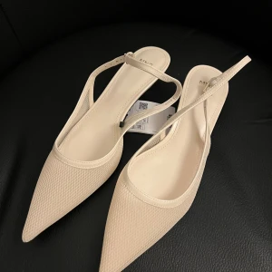 Beige spetsiga pumps från mango - Snygga pumps från mango i beige med spetsig tå och låg klack. Skorna har ett mesh-liknande material på ovansidan och smala remmar med spänne runt hälen. Perfekt för dig som gillar stilrena och trendiga detaljer.