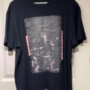 Svart Off-White t-shirt med tryck - Svart t-shirt från Off-White med stort konstnärligt tryck framtill och ikoniskt vitt grafiskt tryck med texten 'WHITE' på ryggen. Klassisk rund hals och korta ärmar. Tillverkad i mjuk bomull som känns skön mot huden.