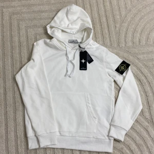 Vit hoodie från Stone Island - Vit hoodie från Stone Island med klassisk logotyp-patch på vänster ärm. Tröjan har huva med snörning. Storlek S passar mer som S/M helt ny oanvänd 10/10 skick, säljer den för den inte passar mig annars den är rikligt fet 💯