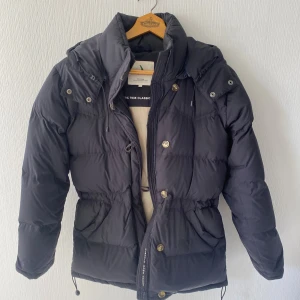 Boomerang dunjacka - Säljer min Boomerang-jacka i modellen The Authentic 7035 Classic Down Jacket. Perfekt vinterjacka med klassisk Boomerang-design och justerbar midja för snygg passform. Det här är en klassisk, tidlös dunjacka från Boomerang perfekt kombination av värme, kvalitet och stil. Färg: Mörkblå Storlek: S Fyllning: Äkta dun – varm men lätt Nästintill nyskick, inga skador eller fläckar