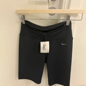 Svarta cykelshorts från Nike nya  - Svarta, tighta cykelshorts från Nike med hög midja och diskret logga framtill. Snygg, minimalistisk design i stretchigt material som passar perfekt till träning eller sportiga outfits. Klassisk look med bekväm passform och elastisk midja.