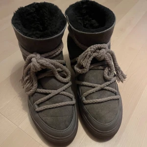 Bruna Inuikii skor - Säljer ett par bruna Inuikii skor med svart ullfoder och grova beige snören. Skorna har rund tå, platt sula och är tillverkade i mocka och skinn. Perfekta för kalla dagar med sin varma insida och snygga design.