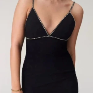 Svart kort klänning ADOORE - Supersnygg svart kort klänning från ADOORE med tunna axelband och djup v-ringning. Klänningen har stendetaljer längs urringningen och nederkanten, samt en figurnära passform!Perfekt till nyårsfirandet! Helt ny med lappar på, säljes pga dessvärre för liten för mig.