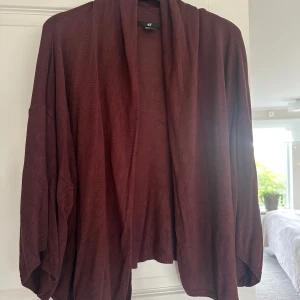 Mörk vinröd kofta från H&M, stl M - Oversized, öppen kofta i mörk vinröd färg från H&M. Tillverkad i en mjuk blandning av viskos, polyamid och angora som ger en skön känsla. Koftan har långa ärmar och ett avslappnat fall utan knäppning, perfekt för lager-på-lager.