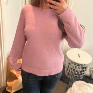 Ljusrosa stickad tröja Vero Moda - Supermysig ljusrosa stickad tröja från Vero Moda. Tröjan har rund halsringning, ribbade muddar och lång ärm. Perfekt för lager-på-lager och chill dagar. Enkel och stilren design som är lätt att matcha med jeans eller kjol.