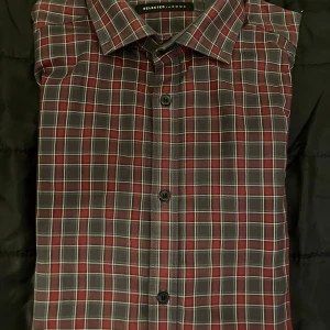 Rutig skjorta från Selected Homme - Snygg rutig skjorta från Selected Homme i mörkröda och grå toner med vita linjer. Klassisk krage, knappar framtill och långa ärmar med manschett. Perfekt för dig som gillar stilrena och tidlösa mönster. Materialet är mjukt och känns skönt mot huden.