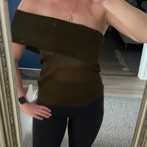 Offshoulder topp  - Säljer en olivgrön offshoulder topp från Massimo Dutti i storlek L. Toppen är ribbad och stickad, med en snygg asymmetrisk axelbandslös design som ger en cool vibe. Materialet är lätt och stretchigt, perfekt för att styla med smycken eller lager på lager.