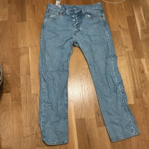 Levi's 501 ljusblå jeans W31 L30 - Klassiska Levi's 501 jeans i ljusblå tvätt med raka ben och knappgylf. Jeansen har fem fickor och den ikoniska läderpatchen bak i midjan. Perfekt för dig som gillar tidlös stil och vill ha ett par jeans som funkar till allt.