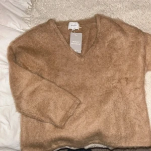 Beige fluffig tröja  - Supermjuk och fluffig beige tröja i mohair- och ullblandning. Tröjan har v-ringning och långa ärmar, perfekt för kyliga dagar. Enkel och stilren design som är lätt att matcha med olika outfits.
