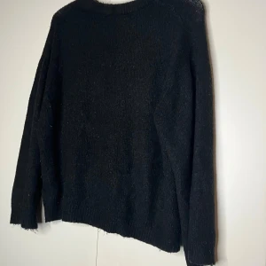 Svart stickad tröja med rund hals - Enkel svart stickad tröja med rund hals och långa ärmar. Tröjan har en klassisk passform och ribbade muddar vid ärmslut och nederkant. Perfekt att slänga på sig när det är kyligt ute.