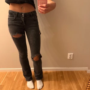 Svarta ripped jeans med bootcut - Säljer ett par svarta jeans med slitna hål vid knäna och klassisk femficksdesign. Lågmidjadejeans från Zara med slitningar och jag är 170 och har storlek 25-27 och 32-34 och xs-s för referens💓