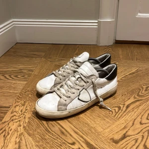 Philippe Model vita och grå sneakers - Snygga sneakers från Philippe Model i vitt och grått skinn med svarta detaljer på hälen. Skorna har snörning med logotyp på skosnörena och en klassisk låg siluett. Perfekta för dig som gillar en avslappnad men trendig stil. de är även  ny sulade de har dock tyvärr gått upp lite i kanten på visa ställen men det går att fixa. 499 pruta och klart