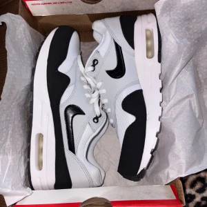 Nike Air Max 1 svartvita sneakers - Snygga Nike Air Max 1 sneakers i svart och vitt med klassisk design. Skorna har en synlig Air-sula, svart swoosh och detaljer i både skinn och mesh för en sportig look. Perfekta för dig som gillar streetstyle och vill ha bekväma sneakers med ikonisk vibe.