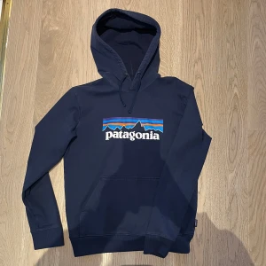 Patagonia Hoodie - Säljer en mörkblå hoodie från Patagonia med klassiskt logotryck i färg framtill. Tröjan har huva med snörning, känguruficka och långa ärmar.