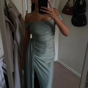 Ljusgrön offshoulder långklänning - Snygg ljusgrön långklänning med offshoulder och draperad överdel. Klänningen har en hög slits framtill. Materialet är glansigt och faller fint längs kroppen, perfekt för en elegant look. Aldrig använd! 💚