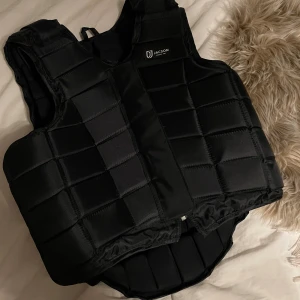 Helt ny oanvänd svart skyddsväst från Jacson - Helt ny oanvänd skyddsväst från Jacson i helsvart med quiltad design och gömd dragkedja framtill. Västen har justerbara remmar och är tillverkad i slitstarkt syntetmaterial. Perfekt för ridning och ger bra skydd över bröst och rygg. Nypris 1300kr och säljer för 899 då den inte har några defekter alls men pris kan eventuellt diskuteras.