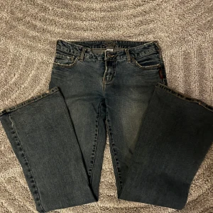 Blå bootcut jeans från Silver Jeans - Snygga lågmidjade blå jeans från Silver Jeans med klassisk bootcut-modell. Jeansen har fem fickor, slitna detaljer och kontrastsömmar. Materialet är mjukt denim med lätt tvättad look och subtila slitningar framtill och baktill. Perfekta för en avslappnad och trendig stil.