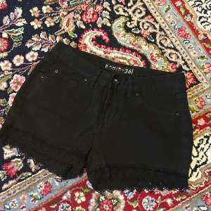 Svarta shorts med spetskant från Amisu - Snygga svarta shorts från Amisu med klassisk femficksmodell och dekorativ spetskant längst ner. Gjorda i mjuk bomull med en touch av stretch för skön passform. Perfekta för varma dagar när du vill ha en stilren look med lite extra detalj.