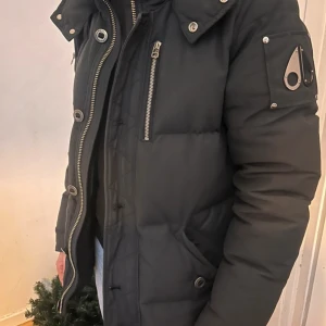 Svart jacka Moose Knuckles -  svart jacka från Moose Knuckles med  logga på ärmen och broderad ryggdetalj. Jackan har dragkedja, stora knappar och flera fickor. Perfekt vinterjacka. Priset går att diskuteras vid en snabb afffär . Jackan har pälskrage som är borttagbar utefter preferens 