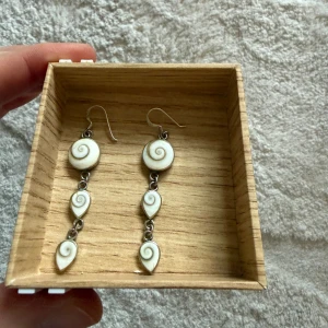 Långa örhängen med snäckspiral. Silver 925 - @ Unika långa örhängen med tre vita snäckformade hängen i spiralform.  @ Använda 2 gånger, är som nya.  @ Silver 925. Köpte utomlands. Hög kvalité. @ Örhängena har silverfärgade krokar och detaljer, och varje hänge har en snygg swirl-design. @ Perfekta för dig som gillar naturinspirerade accessoarer.  Djurfritt och rökfritt hem.