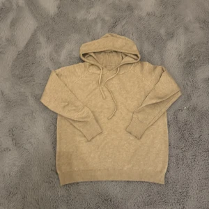 Beige merinoull hoodie  - Säljer en beige hoodie med huva och snörning. Tröjan har långa ärmar, ribbade muddar och en avslappnad passform. Perfekt för dig som gillar en enkel och stilren look. Materialet känns mjukt och skönt mot huden.