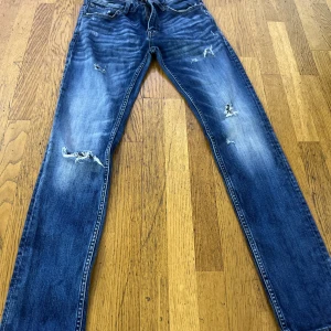 Blå slitna jeans G-Star Raw 502 Slim - Säljer ett par blå jeans från G-Star Raw, modell 502 Slim. Jeansen har slitna detaljer och hål på benen för en cool, avslappnad look. Klassisk femficksmodell med dragkedja och knapp. Perfekta för dig som gillar streetstyle.