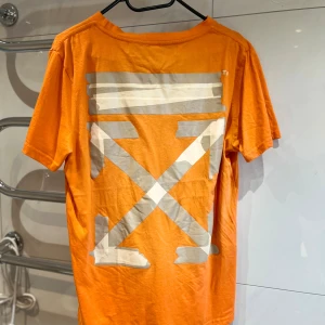 Orange Off-White t-shirt med tryck - Snygg orange t-shirt från Off-White med ikoniskt stort grafiskt tryck i vitt och grått på ryggen och mindre logga framtill. Klassisk passform och rund hals. Tillverkad i mjuk bomull, perfekt för dig som gillar streetwear och vill sticka ut.