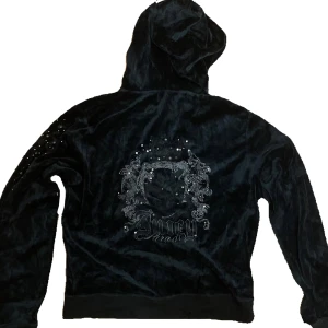 Svart hoodie Juicy Couture - Säljer en svart hoodie från Juicy Couture med glittriga detaljer och tryck på ryggen. Tröjan har huva, dragkedja framtill och fickor. Perfekt för dig som gillar 2000-talsvibe.