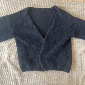 Mörkblå stickad kofta - Mysig mörkblå stickad kofta med avslappnad passform och lång ärm. Perfekt att slänga på sig över en t-shirt eller topp för extra värme. Enkel och stilren design utan knappar eller dragkedja.