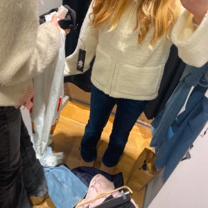 Vit teddyjacka med dragkedja - Mysig vit teddyjacka med hel dragkedja framtill och hög krage. Jackan har en fluffig och mjuk yta i fleece, perfekt för kyliga dagar. Långärmad och med en enkel, clean look som är lätt att matcha med jeans eller leggings.Jättebra skick