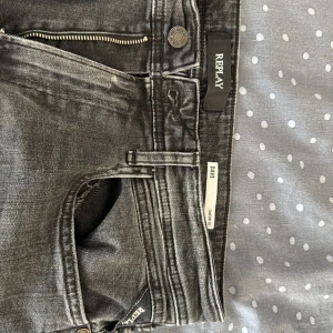 Replay grå jeans Dave modell 33/32 - Snygga Replay jeans i modellen Dave, i en tvättad grå färg med klassisk femficksdesign och dragkedjegylf. Jeansen har Replay-logga på bakfickan och svart patch bak i midjan. Tillverkade i bomull med en skön passform och raka ben. 
