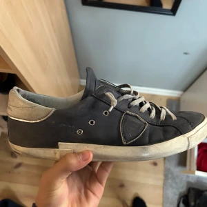 Ett par feta Philippe Model i blå! - Snygga sneakers från Philippe Model i mörkblå skinn med ljusgrå detaljer och snörning. Skorna har en vit sula med svarta undersidor och klassisk låg profil. Perfekta för dig som gillar stilrena och exklusiva sneakers med en urban vibe.