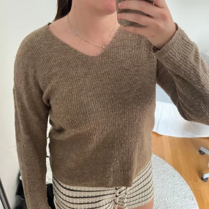 Brun ribbad stickad tröja med v-ringning - Mysig brun stickad tröja med ribbad struktur och v-ringning. Tröjan har lång ärm och en avslappnad passform, perfekt för lager-på-lager under kyligare dagar.