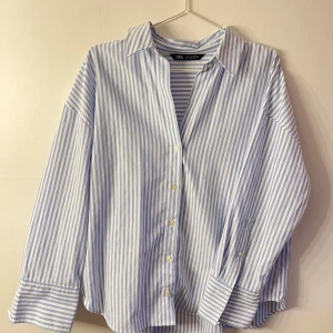 Randig skjorta  - Snygg skjorta från Zara med blå och vita ränder, klassisk krage och knappar framtill. Skjortan har långa ärmar med breda manschetter och en avslappnad passform. Perfekt för en chill och stilren look.