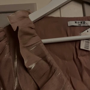 Champagnefärgad omlottblus  - Säljer en glansig champagnefärgad omlottblus från NA-KD med volangdetaljer längs v-ringningen och knyt i midjan. ❤️❤️