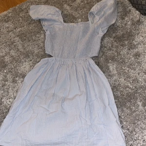 Ljusblå klänning från Kappahl - Supersöt ljusblå klänning från Kappahl med puffiga korta ärmar och smockad överdel. Kjolen är lätt utställd och tyget har en diskret randig struktur. Knappt använd