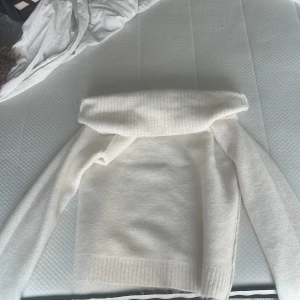 Offshoulder cremefärgad stickad tröja - Superfin cremevit stickad tröja med bred offshoulder-krage. Tröjan har lång ärm och ribbade muddar vid ärmslut och nederkant. Perfekt för dig som vill ha en mysig och trendig look i höst och vinter.