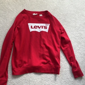 Röd Levi's sweatshirt med logga - Röd sweatshirt från Levi's i storlek S med klassisk vit logga framtill. Tröjan har rund halsringning och långa ärmar. Tillverkad i mjuk bomullsmix, perfekt för en avslappnad och cool stil.