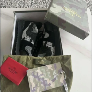 Valentino Rockrunner sneakers camouflage - Snygga Valentino Rockrunner sneakers med svart, grått och vitt camouflage-mönster. Skorna har svarta detaljer i mocka och mesh, samt en robust svart sula med nitar baktill. Klassisk snörning och cool streetstil – perfekt för dig som vill sticka ut priset är ej hugget i sten.