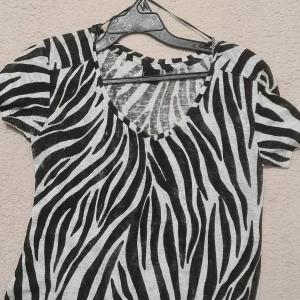 Zebramönstrad t-shirt från KappAhl - Snygg t-shirt från KappAhl i storlek XS med svartvitt zebramönster. Modellen har korta ärmar och en djup v-ringad hals. Materialet är mjukt och lätt, perfekt för dig som gillar att sticka ut med coola mönster. Passformen är normal och t-shirten är riktigt bekväm.