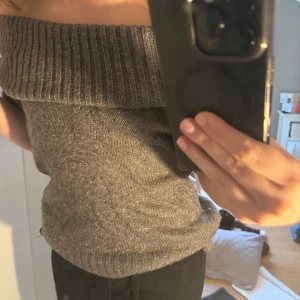 Grå offshoulder stickad tröja - Säljer en snygg grå stickad tröja med bred ribbad kant som sitter offshoulder. Tröjan har korta ärmar och är perfekt för dig som vill ha en trendig och bekväm look. Passar lika bra till jeans som till kjol.